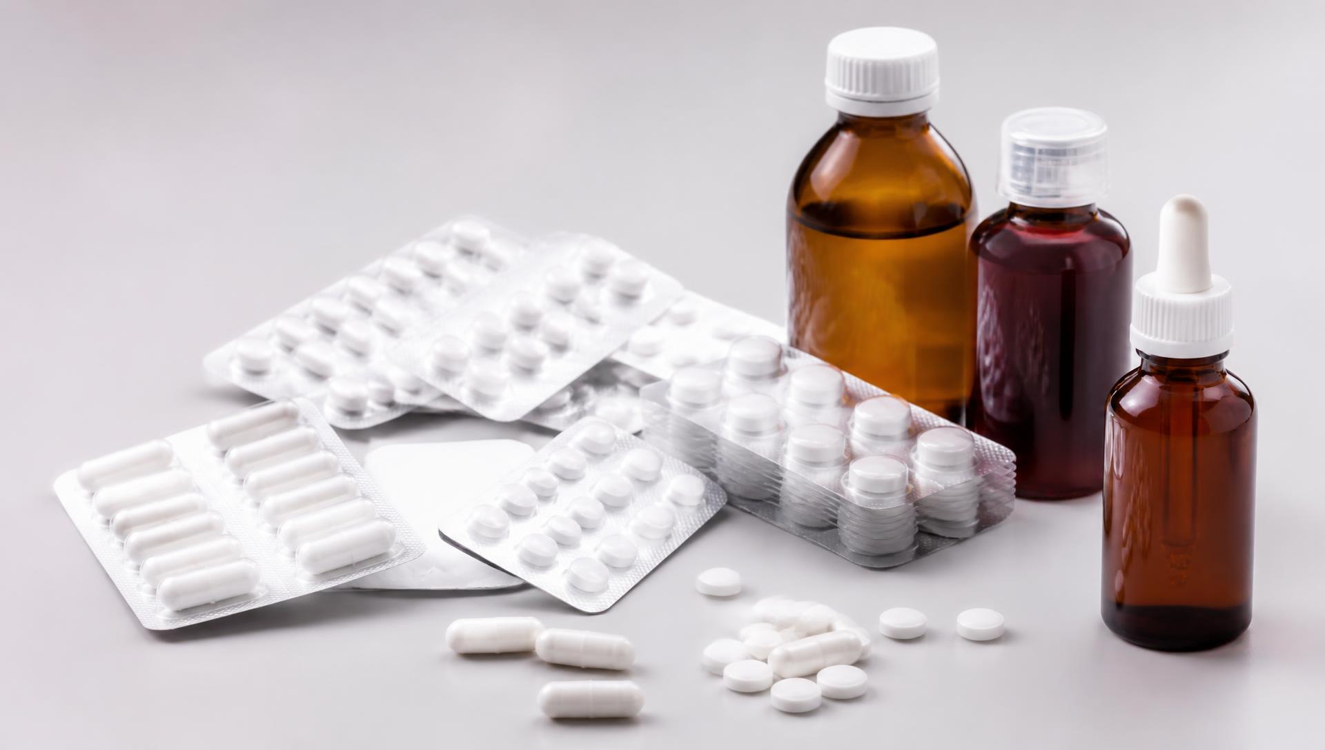 Blister packs of tablets, capsules and syrup bottles arranged on a light surface